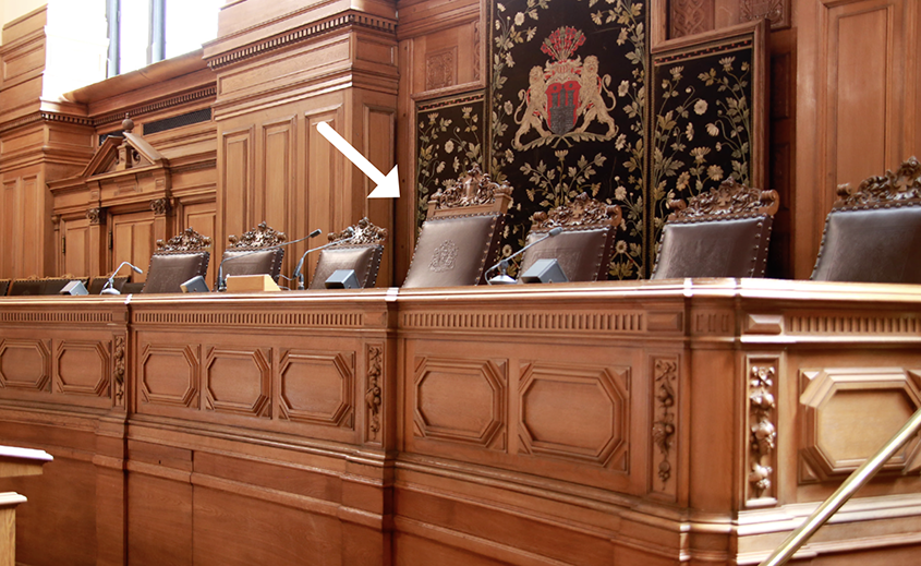Foto von dem mit Holzkassetten verziertem Podest mit dem Stuhl der Bürgerschaftspräsidentin im Plenarsaal des Hamburger Rathauses. Links und rechts vom Stuhl der Bürgerschaftspräsidentin befinden sich jeweils drei weitere Stühle. Sie sind etwas kleiner. Die Rückenlehnen aller Stühle sind mit braunem Leder bezogen. Oben auf den Rücklehnen befinden sich ornamentale Holzschnitzereien. Wobei die Holzschnitzereien am Stuhl der Bürgerschaftspräsidentin opulenter sind. 